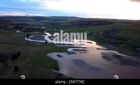 Luftaufnahme eines sumpfigen Geländes im Hintergrund des Sonnenuntergangs am Himmel. Clip. Fluss und Felder biegen Stockfoto