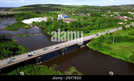 Luftaufnahme eines Flusses und einer Brücke mit Autos an einem Sommertag. Clip. Sommerdorf umgeben von grüner Vegetation Stockfoto