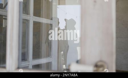 Blick durch das Fenster mit lichtdurchlässigen Vorhängen auf die Menschen in einem Zimmer. Aktion. Weibliche Silhouetten im Gebäude Stockfoto