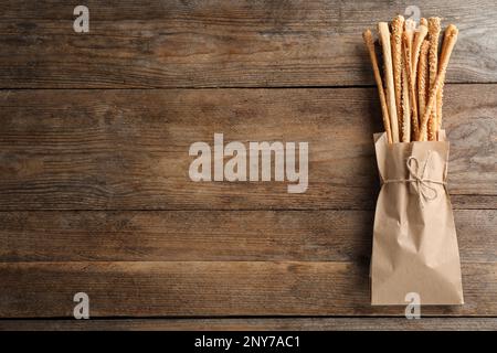 Köstliche Grissini-Sticks in Papiertüte auf Holztisch, Draufsicht. Platz für Text Stockfoto