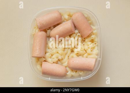 Gekochte Pasta mit Würstchen in einer Kunststoffschüssel auf hellem Hintergrund Stockfoto