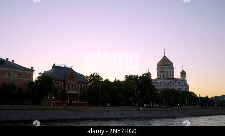 Blick vom Fluss auf den Ufer der Stadt und eine große orthodoxe Kirche. Aktion. Sonnenuntergang über der Stadt und dem Fluss Stockfoto