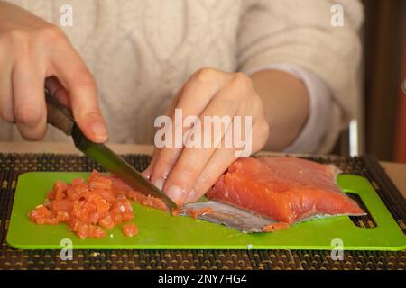 Eine Frau schneidet den Lachs von Hand in Salat auf einem grünen Brett in der Küche Stockfoto