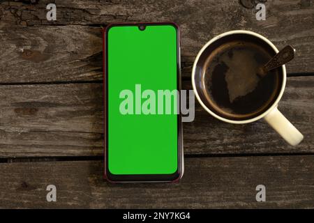 Ein Telefon mit grünem Bildschirm liegt auf einer Tafel und neben einer Tasse Kaffee Stockfoto