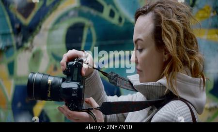 Fotograf, der auf einem Graffiti-Wandhintergrund fotografiert. Aktion. Fotoshooting und Straßenkunst Stockfoto