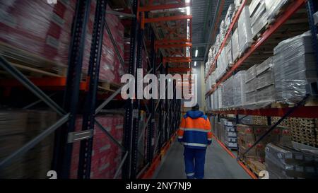 Serbien - Belgrad, 20. September 2022: Innenraum eines großen Fabriklagers mit einem Arbeiter in Uniform, der an den Reihen entlang läuft. Kreativ. Viele Pakete Stockfoto