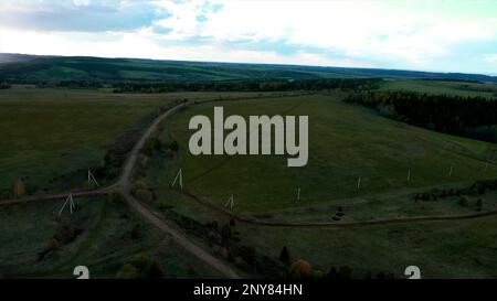 Luftaufnahme einer Landstraße inmitten von grünen, endlosen Wiesen. Clip. Draufsicht auf das Feld und eine schmale Straße mit einem fahrenden Auto Stockfoto