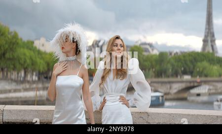 Stilvolle Modelle in weißen Kleidern vor dem Hintergrund der Straßen von Paris und des Effel-Turms. Aktion. Frauen in eleganten Kleidern im Freien, eine davon trägt sie Stockfoto