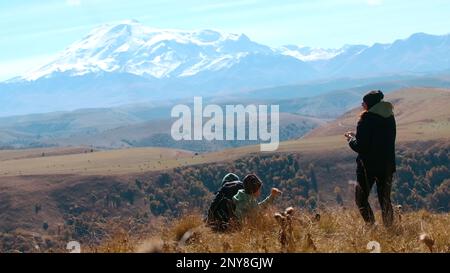 Touristen stehen auf einem Berggipfel und schauen auf schneebedeckte Gipfel. Kreativ. Malerisches Tal im Herbst, Konzept des Tourismus Stockfoto