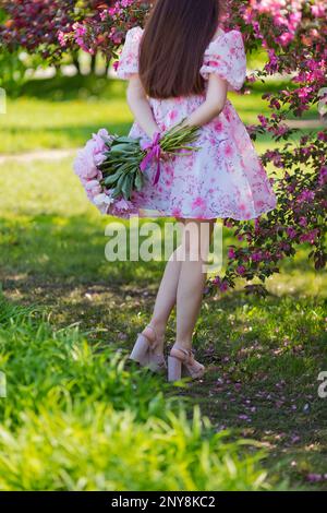 Ein Mädchen in einem rosa Kleid, mit einem großen Strauß Pfingstrosen, Rückansicht Stockfoto