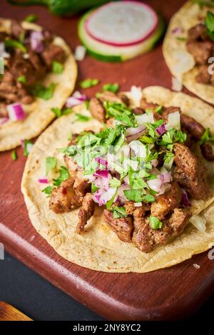 Carne asada Tacos mit verschiedenen Füllungen, serviert auf einer rustikalen braunen Holzplatte Stockfoto