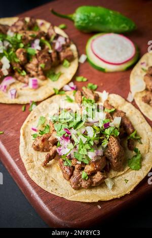 Carne asada Tacos mit verschiedenen Füllungen, serviert auf einer rustikalen braunen Holzplatte Stockfoto