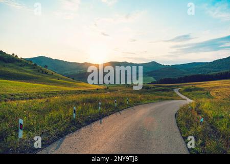 Wunderschöne Bergstraße mit Bäumen, Wald und Bergen im Hintergrund. Eine kleine schmale Straße im Altai-Gebirge. Stockfoto