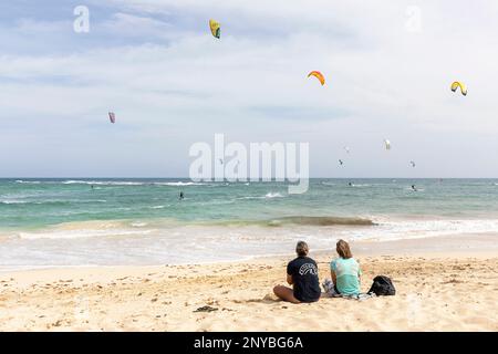 Zwei Touristen schauen auf die Kitesurfer an einem beliebten Kitesurfstrand in der Nähe der Stadt Santa Maria auf der Insel Sal, Cabo verde Archipel Stockfoto