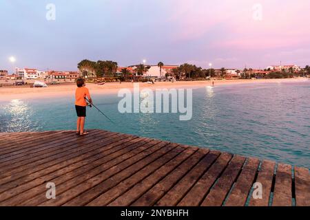 Junge Touristen Angeln auf einem berühmten hölzernen Pier in Santa Maria Stadt auf der Insel Sal kurz nach Sonnenuntergang, Cabo verde Stockfoto