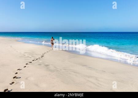 Eine Touristin im Badeanzug, die an einem sonnigen Sommertag auf der Insel Sal, Cabo Verde, an einem idyllischen Sandstrand spaziert Stockfoto