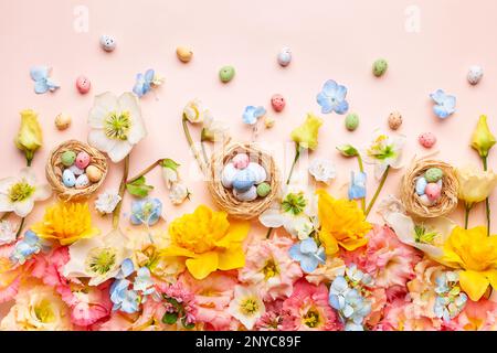 Osterkomposition mit Frühlingsblumen und Ostereiern im Nest auf pastellrosa Hintergrund. Draufsicht, Kopierbereich. Stockfoto