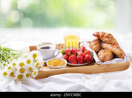 Frühstück im Bett. Tablett mit Tasse Kaffee, Marmelade, Orangensaft, frischem Obst und einem Haufen Gänseblümchen Stockfoto