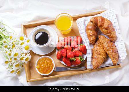 Frühstück im Bett. Tablett mit einer Tasse Kaffee, Orangensaft, frischem Obst und einem Haufen Gänseblümchen, Draufsicht Stockfoto