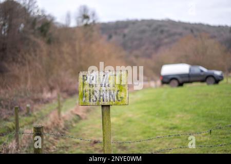 Altes, schäbiges „Private Fishing“-Schild an einem Flusspfad in der britischen Landschaft mit einem Pick-up, der auf einem Feld dahinter geparkt ist. Stockfoto