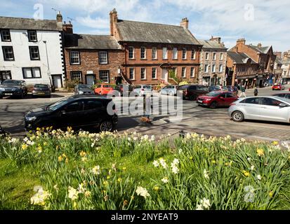 Battlebarrow Street in Appleby in Westmorland Eden Valley Cumbria an einem sonnigen Frühlingstag mit Narzissen blühen und Autos für Shoppers geparkt.Shoppers Stockfoto