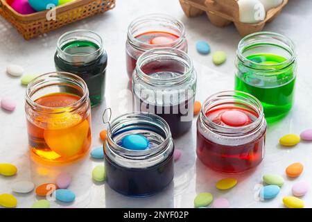 Färben von Ostereiern in farbenfrohen Glasgefäßen mit bunten Osterbonbons auf der Marmortheke Stockfoto