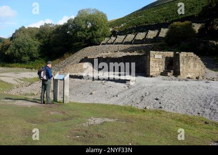 Man (Hiker) sieht sich die Informationstafel über die Überreste der Sir Francis Mine Dressing Floor in Gunnerside Beck, Yorkshire Dales National Park an. Stockfoto