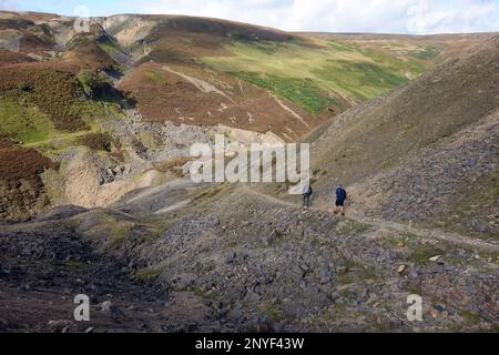 Two Men Walking from the Old Bunton (Bunting) Level Lead Mining Buildings in Gunnerside Gill, Swaledale, Yorkshire Dales National Park, England, Großbritannien. Stockfoto