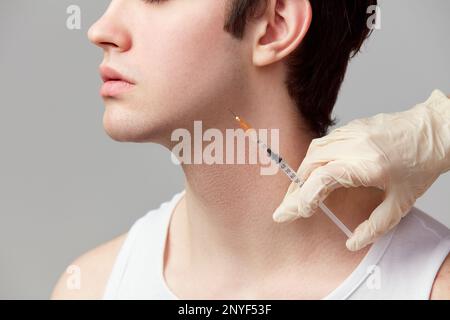Kinnfüllstoffe. Gekürztes Bild eines jungen Mannes, der kosmetologische Injektionen durchführt. Männliches Model vor grauem Studiohintergrund. Konzept von Jugend, Schönheit und Stockfoto