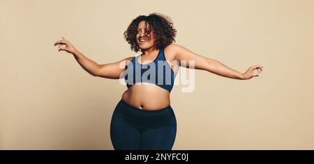 Körperlich selbstbewusste junge Frau, die in Sportbekleidung tanzt und ihre Sportlichkeit und Flexibilität zeigt. Fit in Übergröße Frau, die Spaß hat, wenn sie ihren Körper ausdrückt Stockfoto