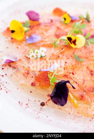 Von oben aus Nahaufnahme des appetitlichen Carpaccio mit Kräutern und Blumen serviert auf weißem Teller Stockfoto