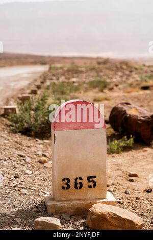 Altes Steinschild mit Zahlen auf rauem felsigem Boden gegen die Straße und wolkenlosem Himmel in Mauretanien Stockfoto