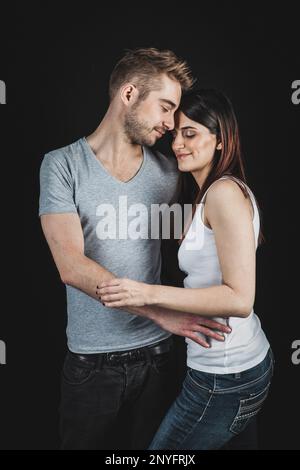 Hübsche Frau und hübscher Mann, der die Augen geschlossen und umarmt Einander auf schwarzem Hintergrund stehend Stockfoto