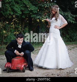 Attraktive junge Braut und Bräutigam lächeln beim Spielen mit alten Spielzeugauto im Garten Stockfoto