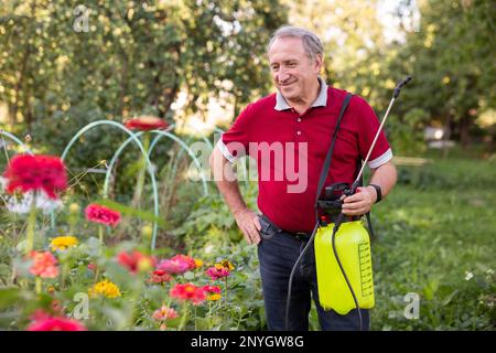Reifer Mann, der beim Lächeln auf Blumen im Garten Insektizid aufträgt Stockfoto
