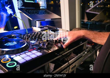 Ein DJ kratzt mit seinen Fingern an der DJ-Kabine. Seine Hand liegt auf dem Mixer und er spielt die Musik in dem Club, in dem die Leute tanzen. Stockfoto