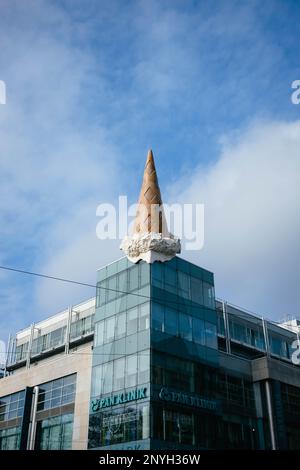 Vertikale Aufnahme eines riesigen Eiskegels auf einem Glasgebäude. Die Eiscreme schmilzt in der Sonne. Im Sommer gibt es Schokolade und Vanille. Stockfoto