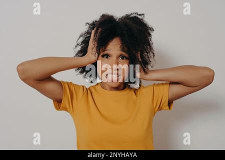 Eine afroamerikanische, verzweifelte junge Frau, die die Kontrolle über Emotionen verliert, ihre Ohren mit den Händen fest schließt und zeigt, dass ich diese Geste nicht mehr ertrage. Stockfoto