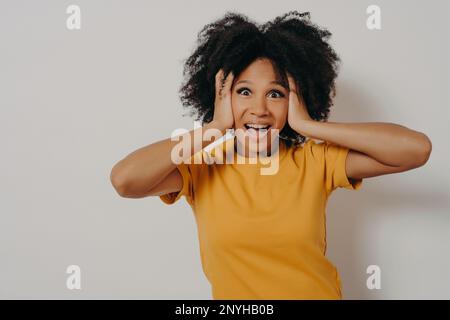 Eine Frau, die mit Armen die Ohren verstopft, möchte keine harte Rockmusik oder laute Musik hören. Eine junge afroamerikanische Frau ignoriert Lärm, der den Kopf mit den Händen bedeckt Stockfoto