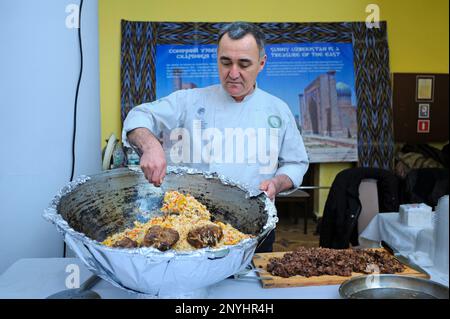 Ein asiatischer Koch kocht usbekischen Pilaf in einem großen Kessel. Festival der orientalischen Kultur. Kiew, Ukraine Stockfoto
