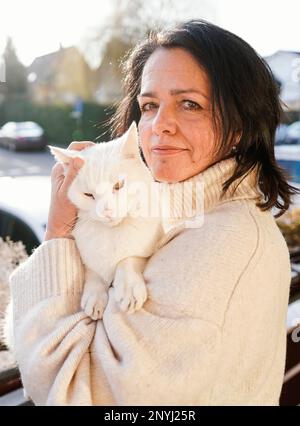 Walldorf, Deutschland. 28. Februar 2023. Die Besitzerin Regine Tredwell steht mit der Katze Fluffy auf dem Balkon ihrer Wohnung. Zum Schutz der vom Aussterben bedrohten Kammbrühe gilt ab April wieder der "Hausarrest" für Katzen in Teilen von Walldorf (Rhein-Neckar-Bezirk). Kredit: Uwe Anspach/dpa/Alamy Live News Stockfoto