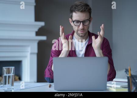 Seriöser fokussierter Online-Lehrer, der auf den Laptop-Bildschirm schaut und spricht, während er von zu Hause aus arbeitet, in lässiger Kleidung gekleidet. E-Learning Stockfoto