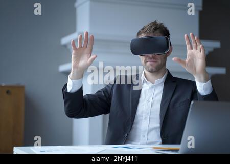 Geschäftsmann, der Technologie der erweiterten Realität im Home Office einsetzt. Man CEO in einer Virtual-Reality-Brille mit erhobenen Händen. Fokussierter Unternehmer i Stockfoto