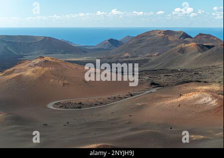 Ariel-Blick auf kurvige Straße, die durch Sanddünen des Timanfaya-Nationalparks mit herrlichen Bergen am Ufer des Atlantischen Ozeans führt Stockfoto