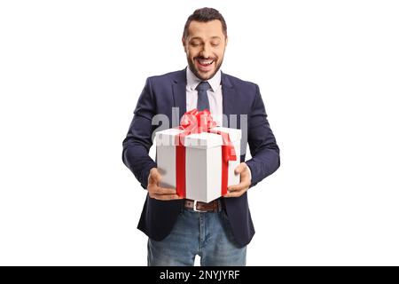 Glücklicher junger Mann in Anzug und Krawatte, der eine Geschenkbox mit rotem Band auf weißem Hintergrund hält Stockfoto