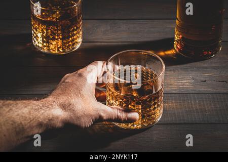 Handgehaltenes Whisky-Glas mit Eis auf Holztisch. Schließen. Stockfoto