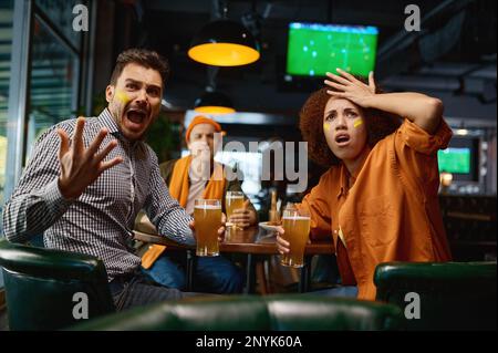 Freunde von Fußballfans mit kreativem Make-up im Pub anfeuern Stockfoto