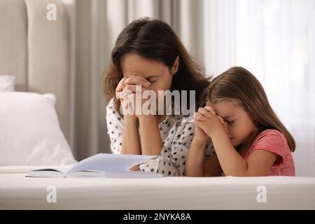 Reife Frau mit ihrer kleinen Enkelin betet zusammen für die Bibel im Schlafzimmer Stockfoto