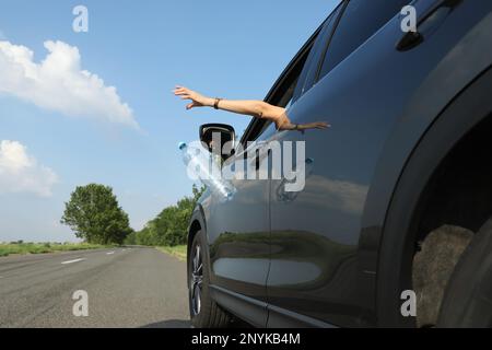 Der Fahrer wirft die Plastikflasche vom Autofenster weg. Müll auf der Straße Stockfoto