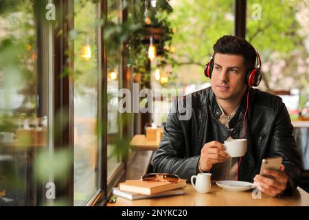 Mann mit Smartphone, der Hörbuch am Tisch im Café hört Stockfoto